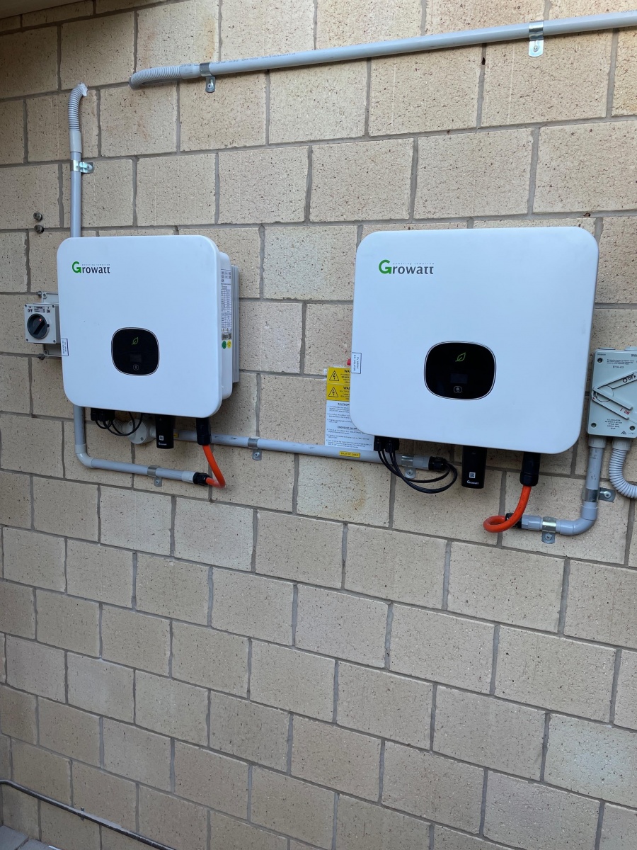 Two wall-mounted solar inverters and isolators installed on the brick wall of a commercial site